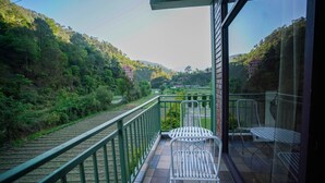A balcony with a view of a forested hillside, a metal railing, and two white chairs. - Kainaat A Riverside Homestay  (Kandaghat)