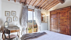 A bedroom with a wooden bed, a desk with a mirror, and a view of the countryside through a window with curtains.