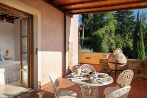 A patio with a table set for tea, surrounded by chairs, and a large urn on a stone wall.