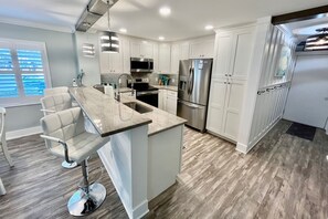 A modern kitchen with white cabinetry, stainless steel appliances, and a bar area with stools.