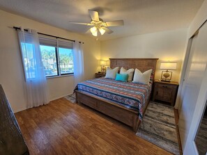 A bedroom with a wooden bed, a ceiling fan, a nightstand with a lamp, and a view of palm trees through the window. - VDL 75 - Relax and enjoy the tranquil lagoon in this 2nd floor condo. (Saint Augustine)