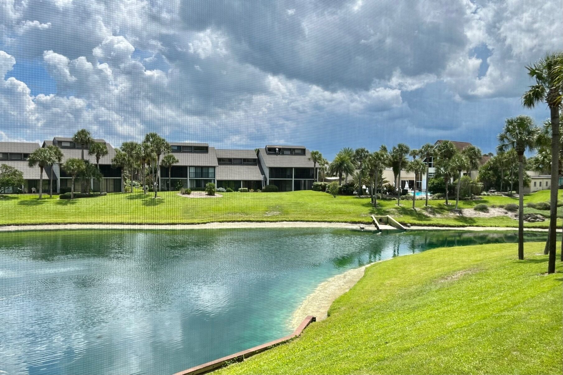 Un ensemble immobilier moderne comprenant une piscine, entouré de pelouses bien entretenues et de palmiers.