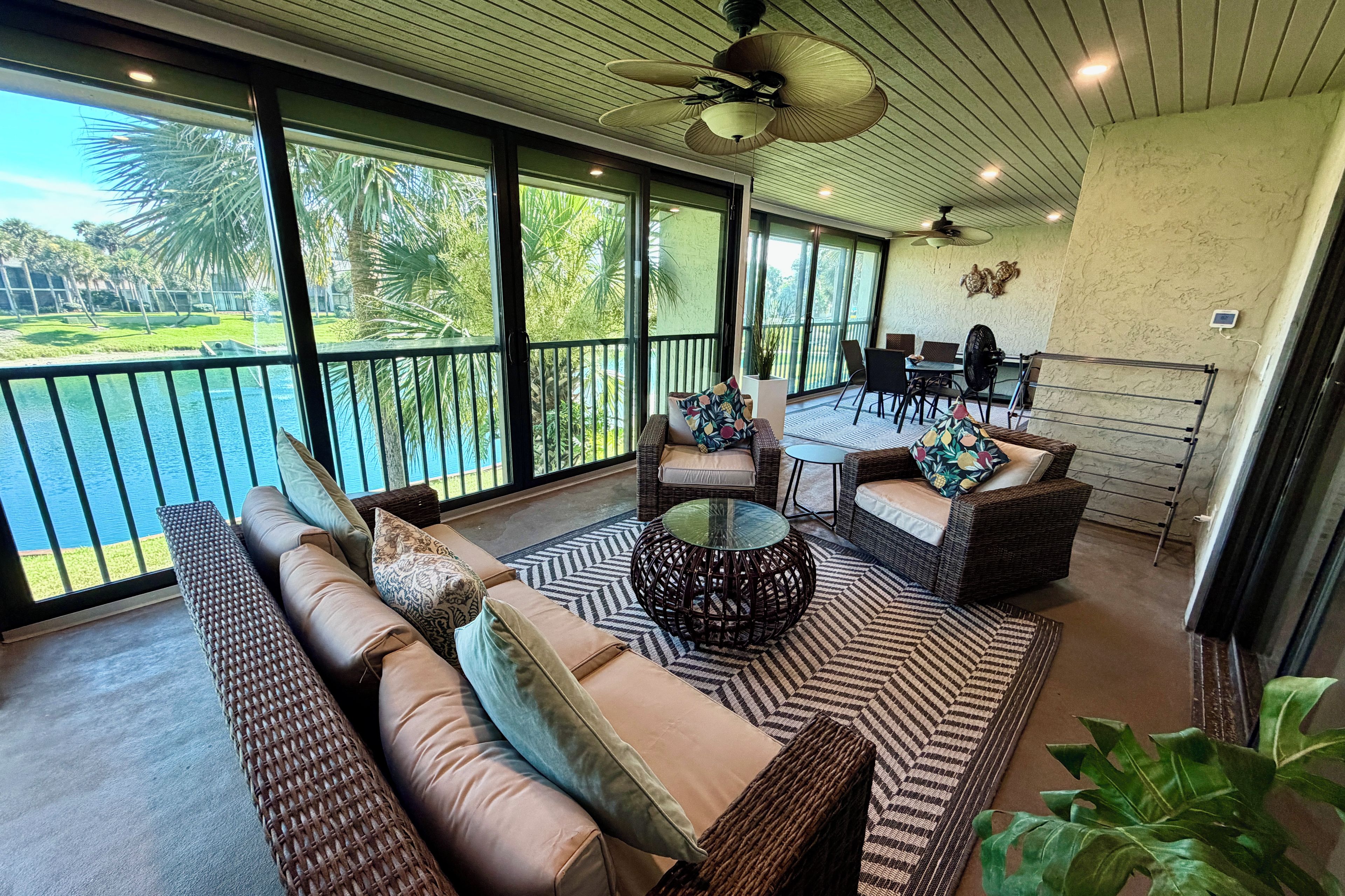 Varanda ampla com vista para uma piscina e vegetação, mobiliada com sofás de vime e uma mesa de centro de vidro.