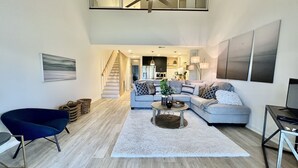 Ein geräumiges Wohnzimmer mit einem modernen Sofa, einem blauen Sessel und einem Couchtisch. Eine Treppe führt in eine obere Ebene.