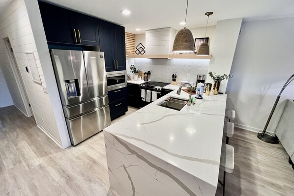 A modern kitchen with stainless steel appliances, a marble countertop, and dark cabinetry.