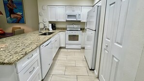 Una cocina con armarios blancos, encimera de granito, microondas, horno y refrigerador.