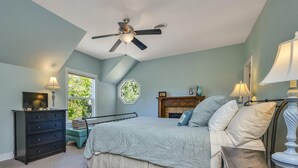 Een slaapkamer met een bed, een dressoir, een plafondventilator, een raam en een open haard.