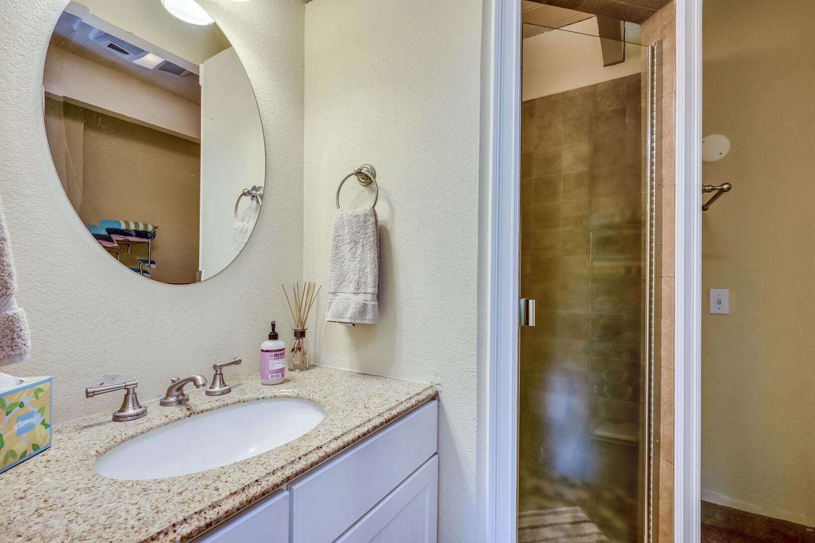 Un baño con lavamanos, espejo, toallero y puerta de ducha.