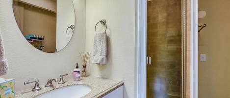 Un baño con lavamanos, espejo, toallero y puerta de ducha.