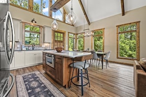A spacious kitchen with a large island, wooden cabinets, and a view of the outdoors through large windows.