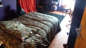 A bedroom with a large bed, a desk with a computer, and a chair.