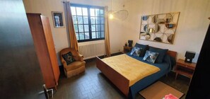 A bedroom with a bed, a chair, a nightstand, a lamp, and a window. - Apartment sur Mer : "Malban" Plage greve blanche (Trégastel)