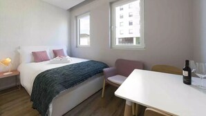Hotellihuone, jossa on sänky, työpöytä, tuoli, pöytä ja pullo viiniä.
