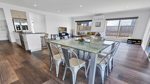 A modern kitchen with a central island, a dining area with a glass table, and a large window providing natural light.