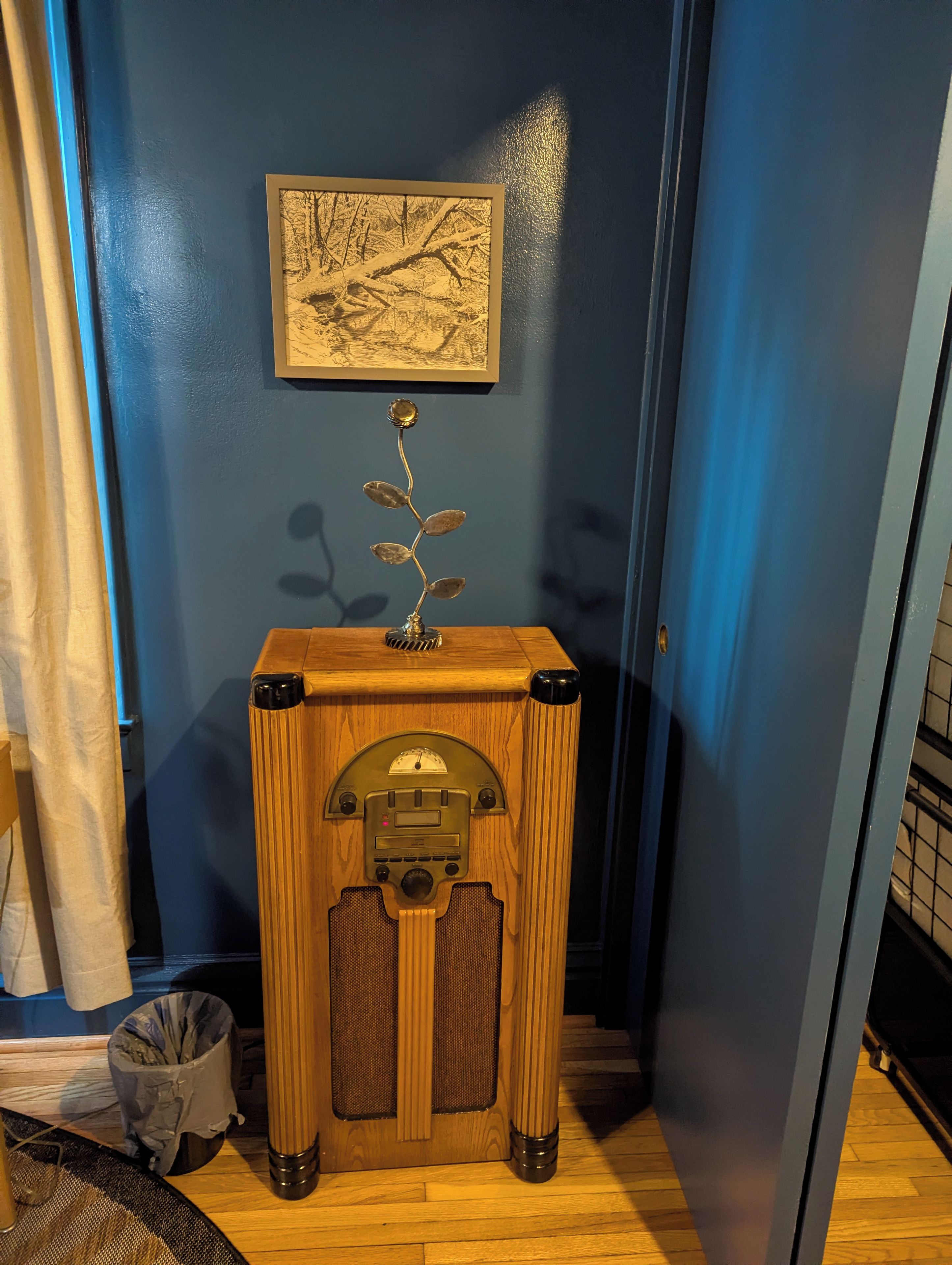 A room with a blue wall, a framed picture, a decorative metal flower, and a vintage radio.