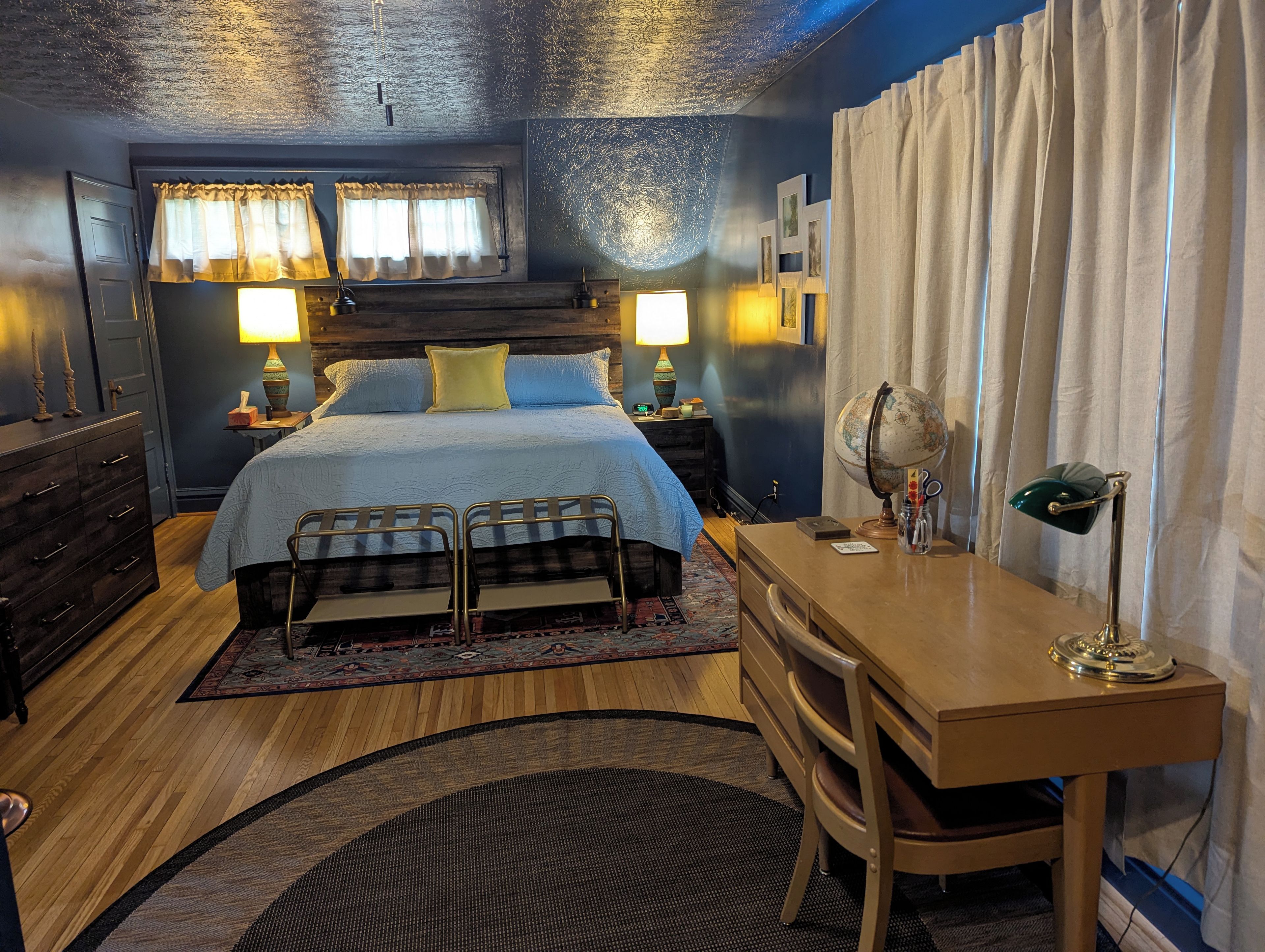 Une chambre à coucher avec un lit, des lampes de chevet, un bureau avec une chaise, un globe terrestre et une fenêtre avec des rideaux.