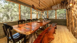 A rustic wooden dining area with a long table, benches, and chairs. - Magical Treehouse on the Brazos River with spiral slide off the deck! 350 acres!  Tubing! (Weatherford)