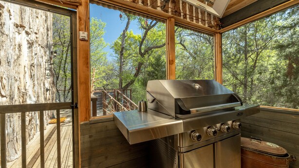 A modern kitchen with a stainless steel grill, large windows, and a wooden deck. - Magical Treehouse on the Brazos River with spiral slide off the deck! 350 acres!  Tubing! (Weatherford)