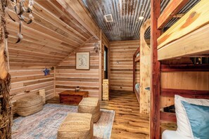 A cozy log cabin interior with a wooden ceiling, a fireplace, and a bunk bed.