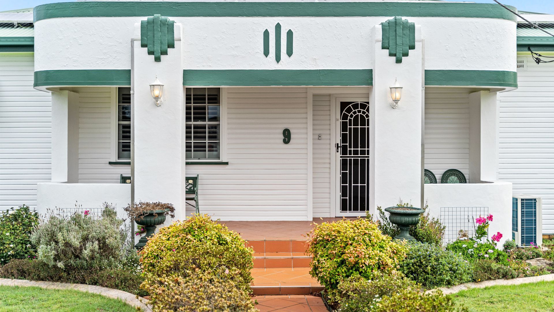 A white building with green trim, a front door, and two potted plants.