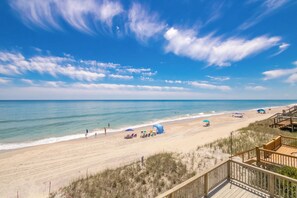 Een strand met een houten looppad, ligstoelen, parasols en een heldere lucht.
