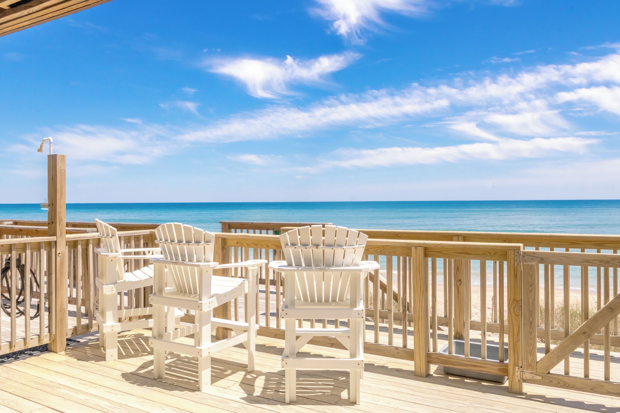 Eine Holzterrasse mit weißen Stühlen mit Blick auf einen Strand.