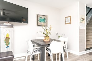 Uma sala de jantar com mesa, cadeiras, um vaso de planta e obras de arte nas paredes.