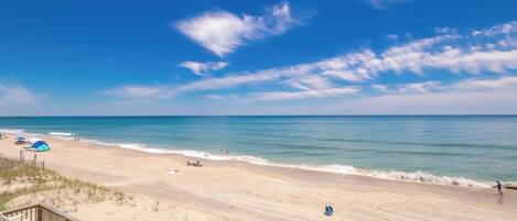 A beach with a wooden boardwalk, umbrellas, and a clear sky.