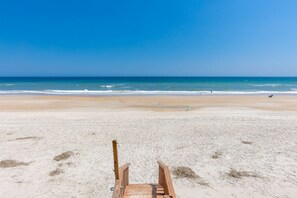 Ein Strand mit einer Holzpromenade, die zum Wasser führt, einem klaren Himmel und einem ruhigen Meer.