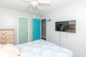 A bedroom with a bed, a dresser, a ceiling fan, a television, and two doors. - Duzzi's Destiny - Oceanfront 5 BR Cottage!  Dog Friendly! (Surf City)