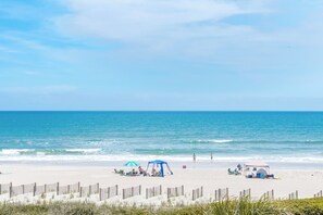 Une plage avec une clôture en bois, des tentes et des chaises de plage.