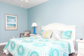 A bedroom with a bed, a nightstand, a lamp, a chair, and a framed picture on the wall.