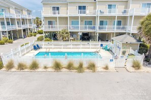 Un hotel de varios pisos con piscina, vallas blancas y vista al mar.