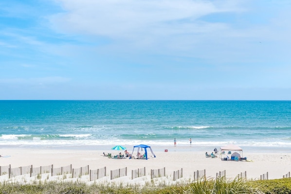 A beach with a sandy shore, a wooden fence, and a clear blue sky.