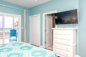 A bedroom with a bed, a TV, a dresser, and a door leading to a balcony.