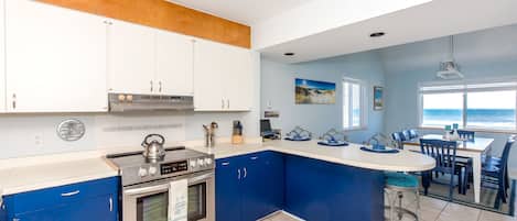 A kitchen with a central island, a dining area with a view, and a beach-themed decor.