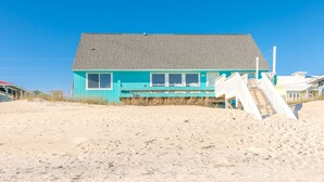 Ein Strandhaus mit geneigtem Dach, einer Veranda mit Stühlen und einer Treppe zum Strand.