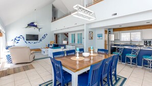 Eine moderne Küche mit Essbereich, ausgestattet mit einem Holztisch und blauen Stühlen, einer Kücheninsel mit Barhocker sowie einem Deckenventilator.