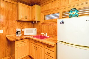 A compact kitchen with wooden cabinets, a white microwave, a red sink, and a white refrigerator.
