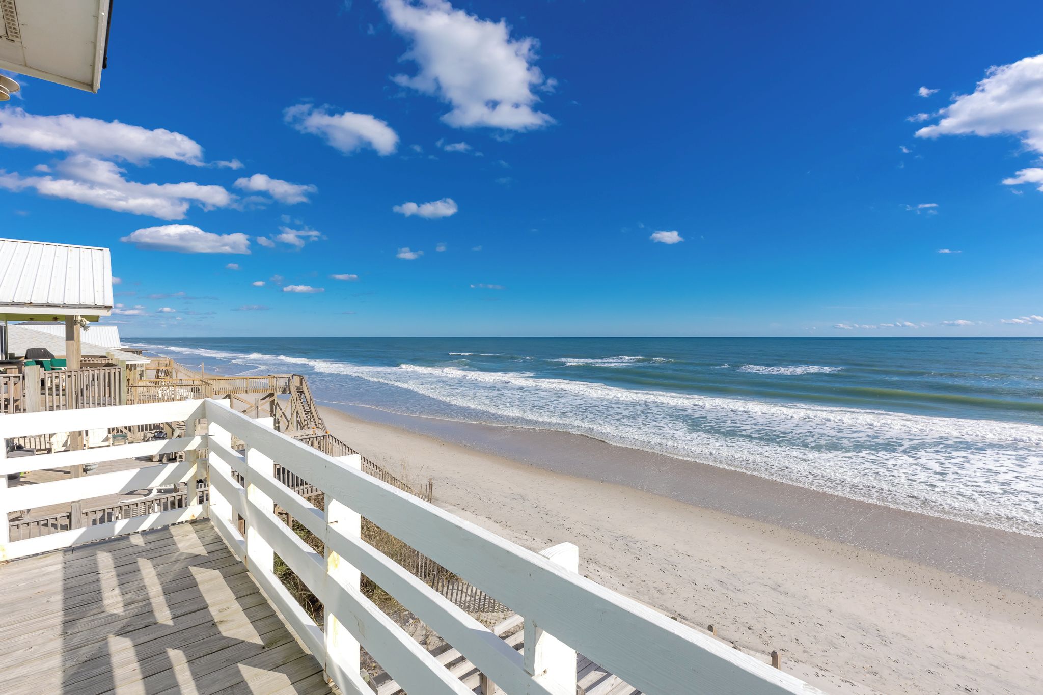 A beach view with a wooden boardwalk leading to a building with a white roof.