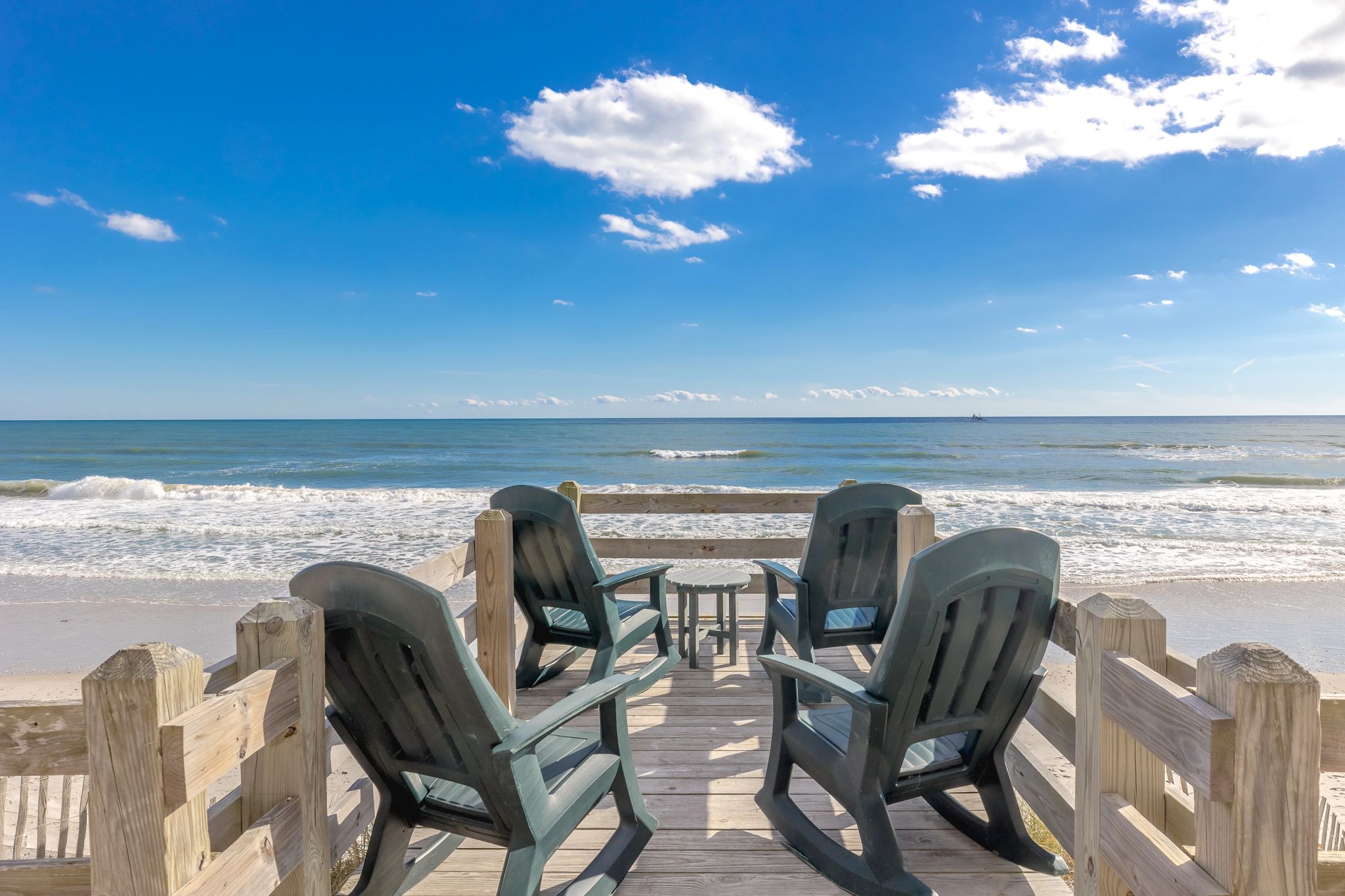 A wooden deck with chairs and a table overlooking the ocean.