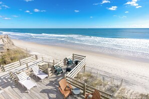A wooden deck with beach chairs and tables overlooking a sandy beach and ocean. - Barefoot Shack - Classic Custom 5BR Oceanfront Home - Great Views from Decks (Surf City)