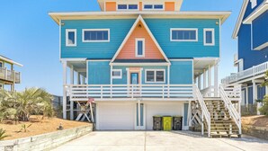 Ein mehrstöckiges Strandhaus mit Garage, einem Balkon und einer Treppe, die zu den oberen Stockwerken führt.
