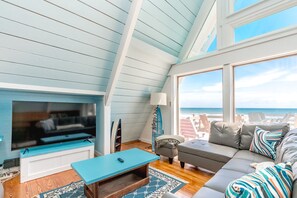A cozy living room with a TV, a sofa, and a view of the ocean. - Barefoot Shack - Classic Custom 5BR Oceanfront Home - Great Views from Decks (Surf City)