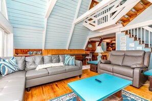 A spacious living room with a grey sofa, a blue coffee table, and a grey recliner. - Barefoot Shack - Classic Custom 5BR Oceanfront Home - Great Views from Decks (Surf City)