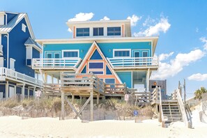 A multi-story beachfront building with a balcony, wooden walkways, and a sandy beach in the foreground. - Barefoot Shack - Classic Custom 5BR Oceanfront Home - Great Views from Decks (Surf City)