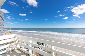 A beach view from a balcony with a railing, overlooking the ocean.