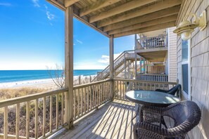 A wooden deck with a glass table and wicker chairs, overlooking a beach.