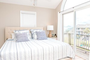 A bedroom with a large bed, a nightstand, a lamp, and a view of a balcony.