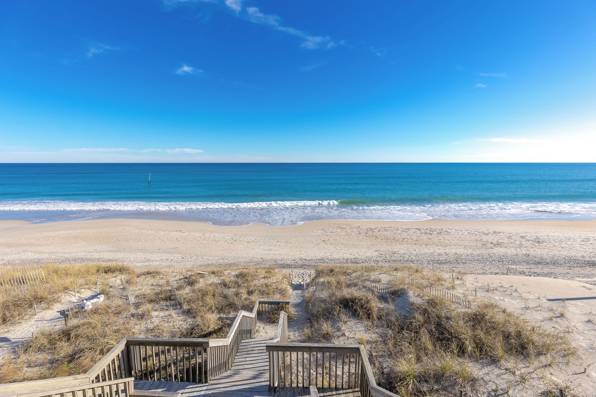A wooden boardwalk leading to a beach with clear skies.